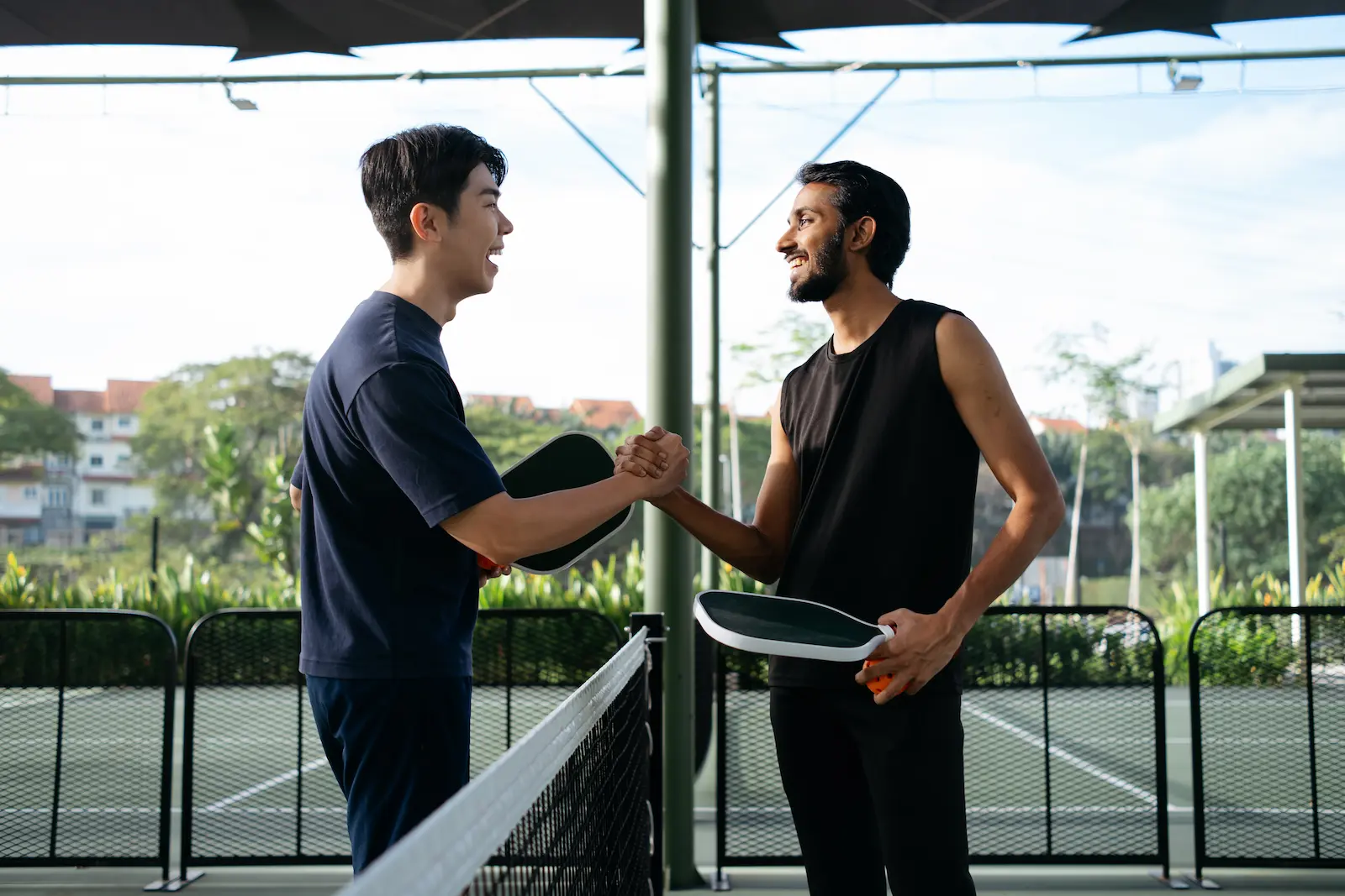Two friends clasping hands over the net on a pickleball court